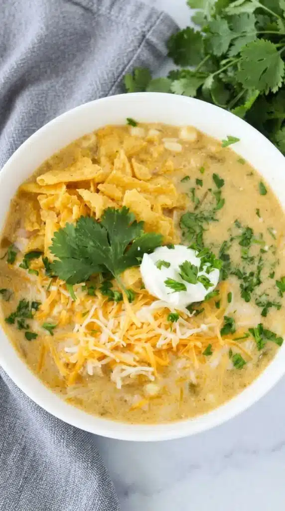 Creamy Green Chile Chicken Enchilada Soup topped with cheese, tortilla strips, and cilantro