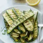 Grilled Zucchini Recipe That Tastes Amazing Fast 11 Grilled zucchini slices with lemon wedges and parsley on a ceramic plate