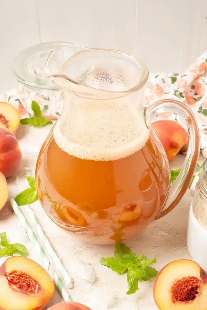 Fresh Southern Peach Tea in a glass pitcher with peaches and mint