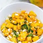 Mango and feta salad with fresh basil and olive oil in a bowl