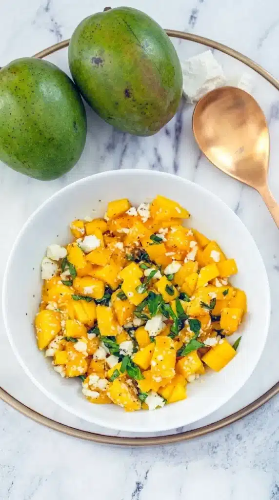 Mango and feta salad in bowl with fresh basil and olive oil