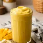 Mango coconut milk smoothie in glass with fresh mango slices and honey
