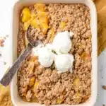 Peach crisp with canned peaches topped with vanilla ice cream in a baking dish