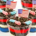 Red White and Blue Dirt Cups with pudding layers, Oreo crumbs, gummy worms, and flag topper