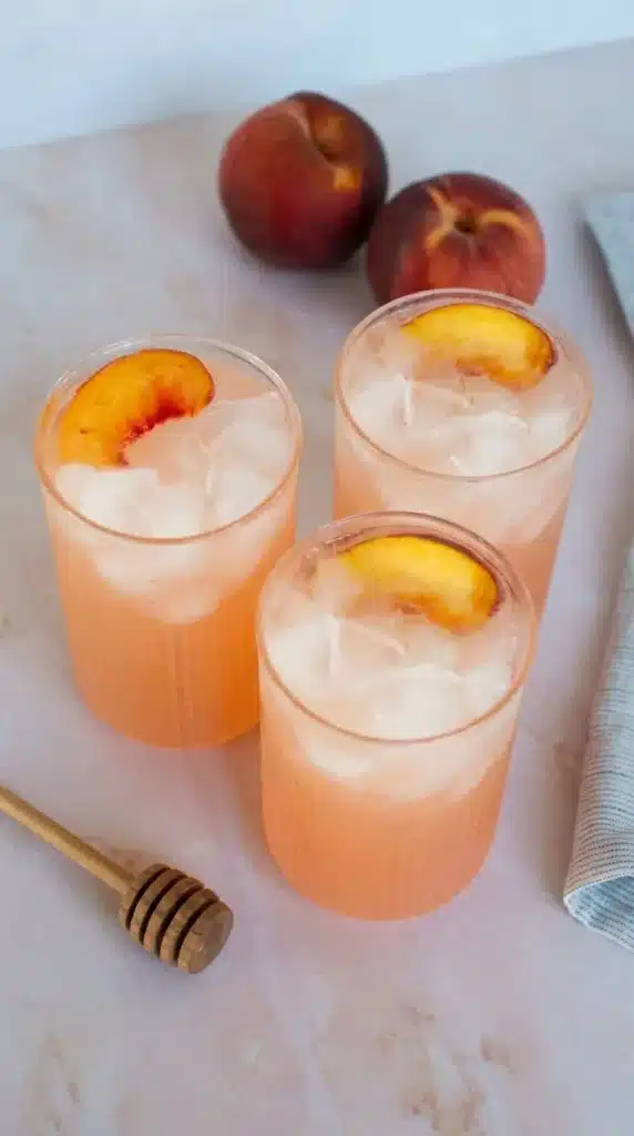 Refreshing peach lemonade with ice and peach slices in textured glasses