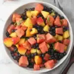Summer fruit salad with watermelon, peaches, blueberries, and fresh basil in a serving bowl
