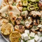 Greek marinated grilled chicken platter with feta, olives, grilled lemon, and flatbread