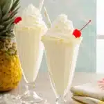 Creamy Pina Colada Milkshakes topped with whipped cream, cherries, and coconut rims