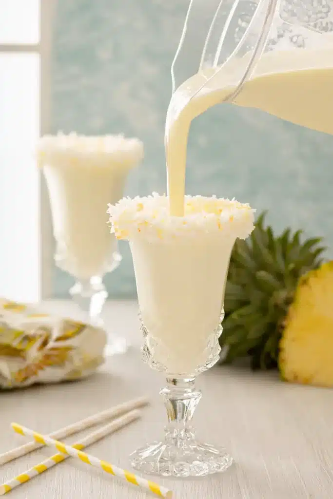 Pouring Pina Colada Milkshakes into coconut-rimmed glasses