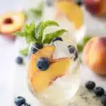 Refreshing Peach Sangria with peaches, blueberries, mint, and ice in a summer cocktail glass