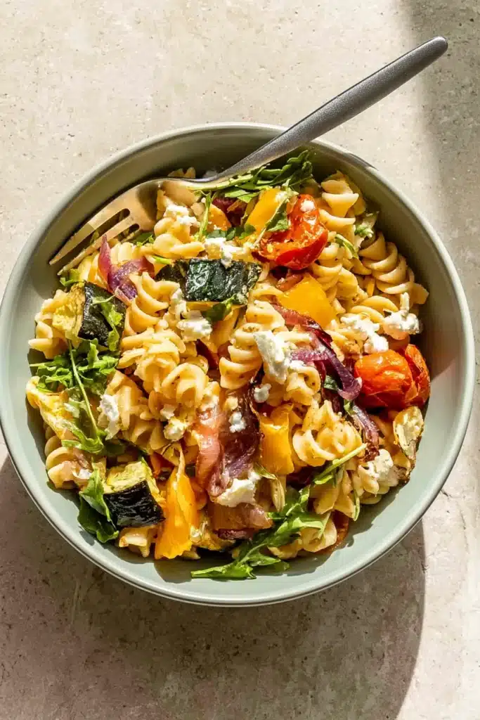 Roasted veggie pasta with feta cheese, zucchini, tomatoes, and arugula in a bowl