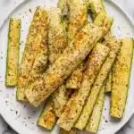 Baked Parmesan Zucchini Recipe | Easy Crispy Family Favorite 7 Baked Parmesan zucchini spears with crispy herb coating served on a ceramic plate.