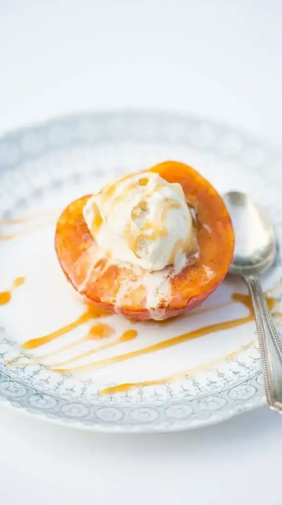 Baked Peaches topped with vanilla ice cream and caramel sauce on a stoneware plate.