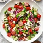 Fresh Greek salad with cucumber, tomatoes, feta, olives, and homemade dressing in a ceramic bowl.