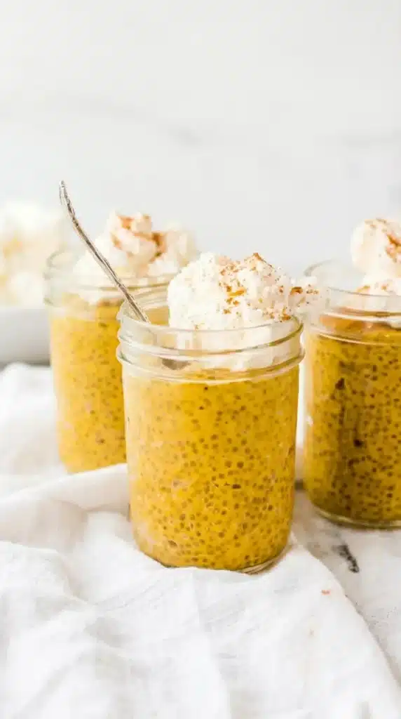 Pumpkin Chia Seed Pudding on a spoon with whipped cream above glass jars.