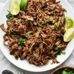Slow cooker Barbacoa with tender shredded beef, cilantro, and fresh lime wedges.