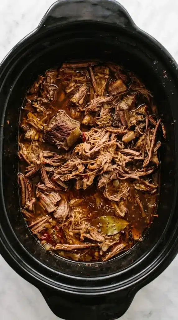 Tender Barbacoa beef cooking in a slow cooker with rich cooking juices.