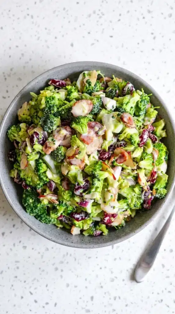 Creamy broccoli salad with bacon, cranberries, almonds, and red onion in a ceramic bowl