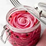 Quick Pickled Red Onions in a glass jar with tangy pink brine and peppercorns