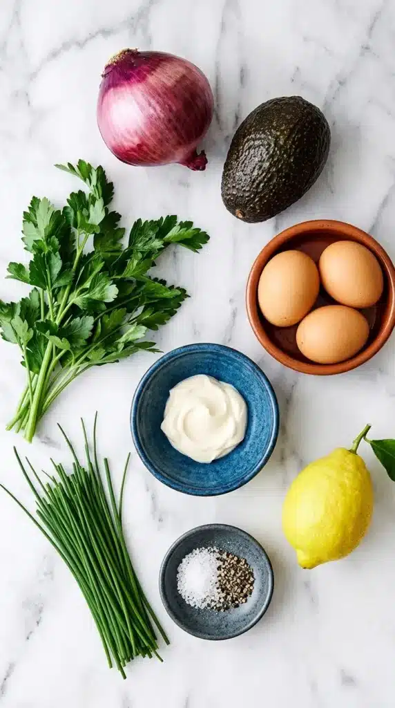 Avocado Egg Salad ingredients with eggs, avocado, red onion, lemon, mayonnaise, chives, and parsley