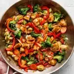 Chicken stir fry with broccoli, bell peppers, carrots, and homemade sauce in a skillet