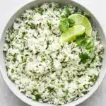 Fluffy cilantro lime rice with fresh cilantro and lime wedges in a ceramic bowl.