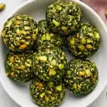 Matcha Pistachio Energy Balls coated with crunchy chopped pistachios on a ceramic plate