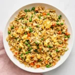 Chinese-style fried rice with eggs, peas, carrots, and green onions in a ceramic bowl.