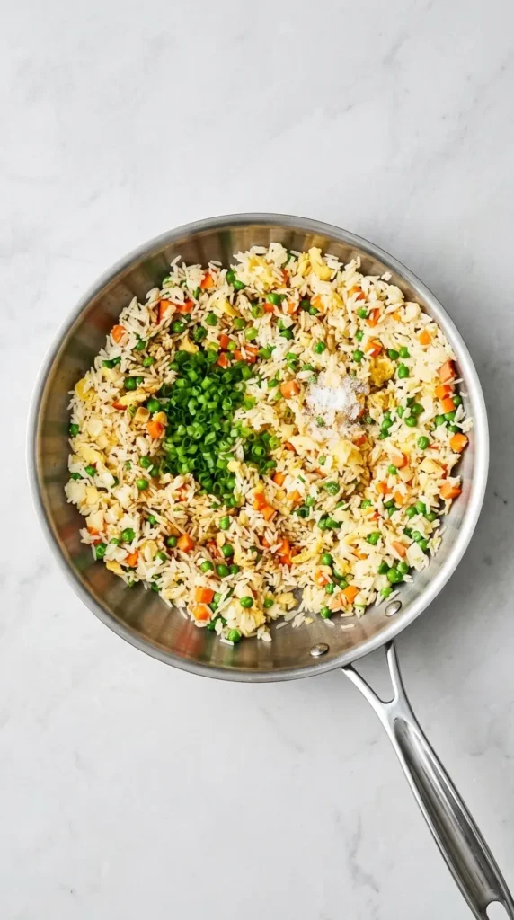 Fried Rice cooking in a wok with eggs, peas, carrots, green onions, and savory seasonings.