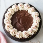 Healthy Peppermint Bark Cheesecake with chocolate ganache, whipped cream, and crushed candy canes