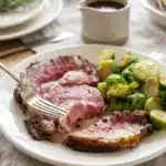 Butter and Garlic Crusted Prime Rib with juicy pink slices, golden herb crust, and roasted Brussels sprouts.