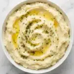 Creamy buttery mashed potatoes with melted butter, fresh chives, and black pepper in a rustic ceramic bowl.