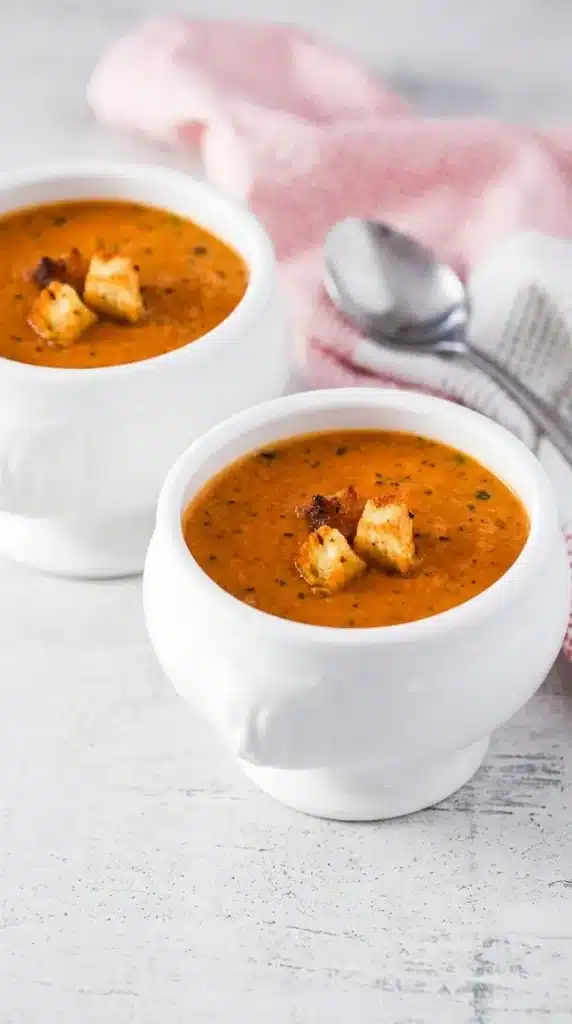 Creamy Roasted Tomato Basil Soup in a rustic ceramic bowl topped with golden garlic croutons and fresh herbs.