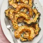 Parmesan Herb Roasted Acorn Squash with golden cheese crust, garlic, and herbs on a ceramic platter