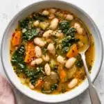 Tuscan White Bean Soup with cannellini beans, kale, carrots, and herbs in a rustic ceramic bowl